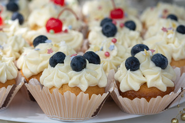 Homemade Cupcakes-muffins with cream cheese frosting, decorated with cherry and fresh blueberries. Selective focus