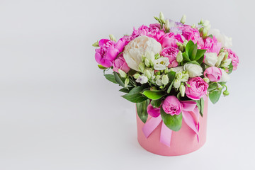 Fototapeta na wymiar Arrangement of flowers in a hat box. Bouquet of peonies, eustoma, spray rose in a pink box with an oasis on a white background with copy space