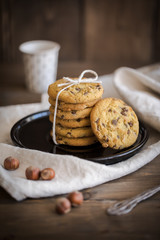 close up of nut and chocolate chip cookies on black plate, linen and brown wooden table, with espresso coffe on background