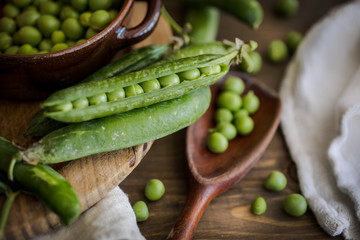 view of some raw fresh green peas in an earthenware plate and some pea pods on a brown rustic wooden table and linen