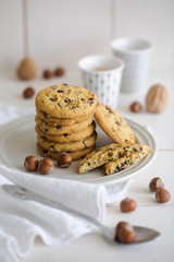 Close-up of nut and chocolate chips cookies on a white plate and linen with bright colors and coffee walnuts and spoon in soft-focus in the background