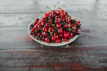 a large plate with berries of sweet cherry and strawberry stands on a dark wooden table