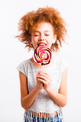 Little curly girl with a big lollipop on a light background.