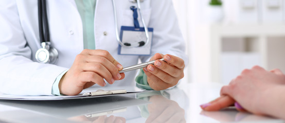 Unknown doctor and patient talking while sitting at the desk in hospital office, close-up of human hands. Medicine and health care concept