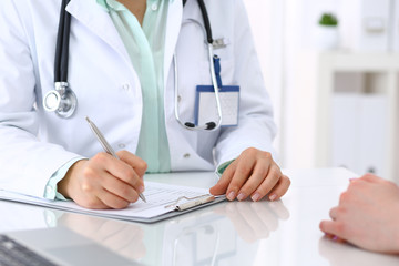 Unknown doctor and patient talking while sitting at the desk in hospital office, close-up of human hands. Medicine and health care concept