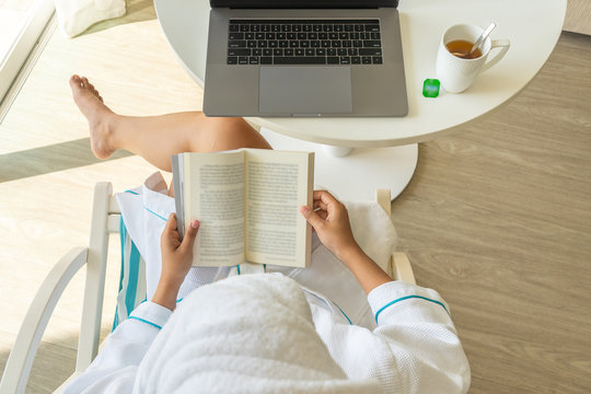Woman wearing bathrobe relaxing by reading book and drinking tea