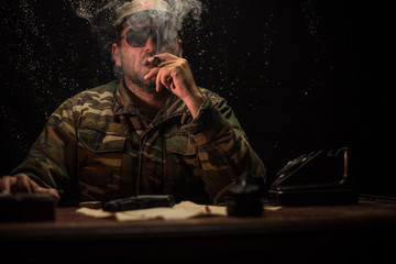 The evil dictator sitting on table. Angry communist general sitting at headquarter or Cuban...