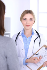 Young woman doctor and patient looking at medication history records while standing straight in hospital Blue colored blouse of therapist looks good. Medicine and healthcare concept