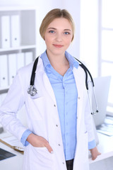 Young woman doctor at work in hospital looking at camera. Blue colored blouse of therapist looks good. Medicine and healthcare concept