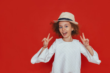 Headshot portrait of little girl with curly hair and blond hat, smiling, looking at camera