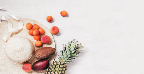 Summer concept female hat with tropic fruit on wooden table copy space top view