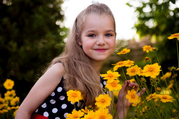 Portrait of a beautiful smiling girl outdoor. Summer portrait of a smiling girl. Little beautiful girl blonde in colors. Garden with yellow flowers, summer girl 
