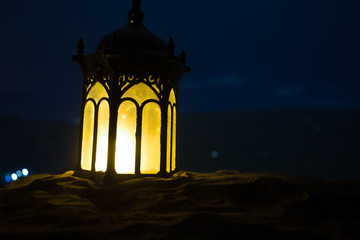 Fototapeta premium Ornamental Arabic lantern with burning candle glowing at night. Festive greeting card, invitation for Muslim holy month Ramadan Kareem.