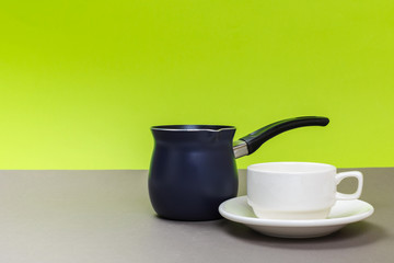 New metal coffee pot and white porcelain cup on a gray table and green background