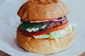 Delicious fresh homemade cheese burger with grilled meat, cheese, tomatoes, lettuce and onion rings in kraft paper. street food on wooden background