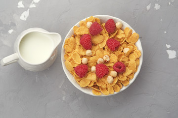Bowl of cornflakes with raspberries, nuts and jug of milk.  Healthy breakfast, top view