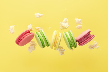 Multicoloured macaroons falling on a light yellow background