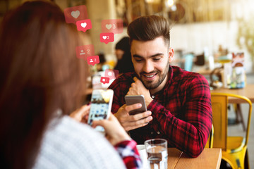 Attractive Caucasian couple dressed casual using smart phones for social media while sitting in cafe.
