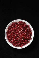 Pomegranate seeds in a bowl on a dark background. Top view