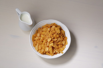 Cornflakes in deep plate and jug of milk on a light wooden table. Top view