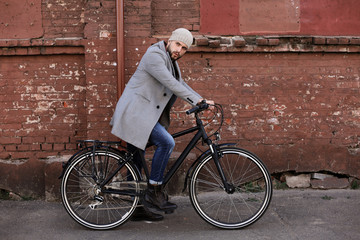 Fototapeta premium Handsome young man in grey coat and hat riding a bicycle street in the city.