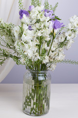 A bouquet of white and lilac flowers in a vase on a wooden table