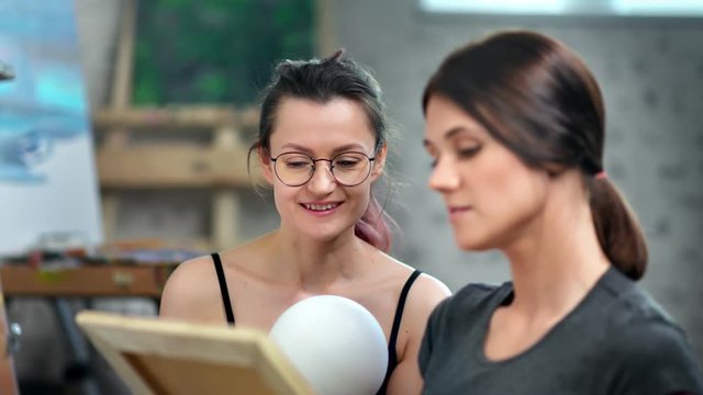 Professional female painter teaching woman student sketching ball at workshop medium close-up