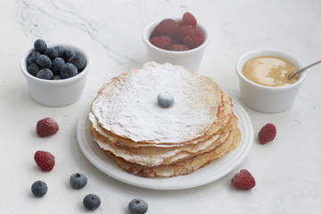 Pancakes with berries sprinkled with powdered sugar on a light marble background