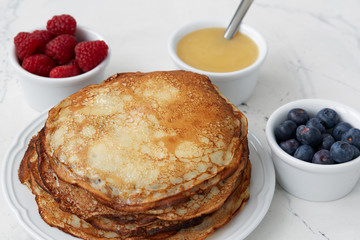 Homemade pancakes or crepes served with honey, raspberries and blueberries on a light background