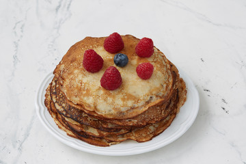 Pancakes served on a plate and decorated with raspberries and blueberries on a light background