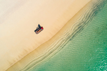 Aerial view of slim woman sunbathing lying on a beach chairin Seychelles. Summer seascape with girl, beautiful waves, colorful water. Top view from drone.