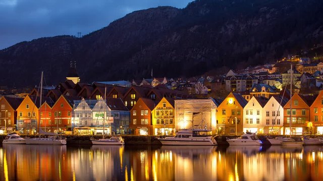 Night time-lapse of colorful houses on a harbor with docked boats and motion blur of moving traffic lights in the Fjords of Norway