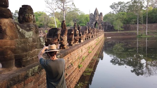 A tourist photographs stone figures of &ldquo;giants&rdquo; of asuras (evil spirits) and devas (good spirits) along a dam crossing the moat at the south gate of Angkor Thom, among the complex of temples of Angkor