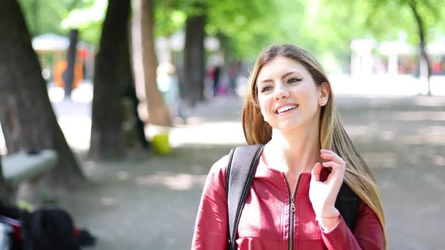 Female student walking outdoor in the park and smiling