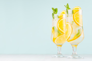 Cold oranges beverage with pieces fruit, ice cubes, mint on elegant soft light green background,...