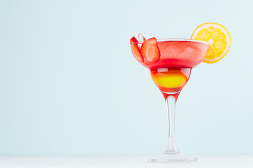 Tropical sunrise striped red, yellow drink with orange, strawberry piece, ice in exquisite misted glass on pastel green background.