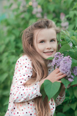 Spring portrait of beautiful smiling little girl with lilac flowers.