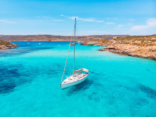 White yacht stands in azure transparent water sea, beach Blue Lagoon Comino Malta. Aerial view