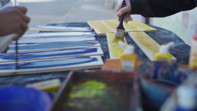 Two teenagers paint wood pieces with color in a local studio