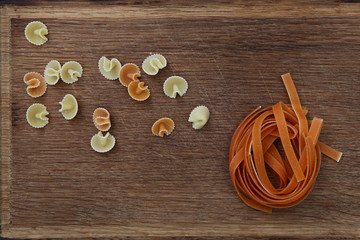 Pasta nest and in assortment of yellow and orange color on a wooden background. View from above. Still life concept.