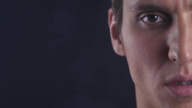 Half face portrait of concentrated young man opens his eyes and looks to camera on black background