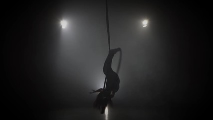 Silhouette young caucasian brunette sportive dancer female balancer in beige leotard back lying hang on aerial hoop on three rays of light background 030