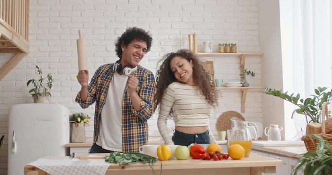 Funny asian couple with curly hair dancing and singing while cooking at kitchen, spending time together - recreational pursuit slow motion 4k