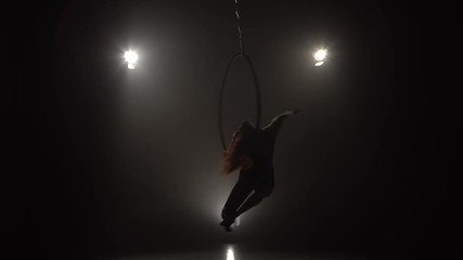 Silhouette young caucasian brunette sportive dancer female balancer in beige leotard back lying hang on aerial hoop on three rays of light background 031