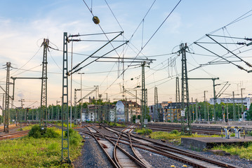 Fototapeta premium Outdoor view of straight and curve railway track lines without train at train station with mess complex electric cables and poles with golden light atmosphere against evening before sunset sky.