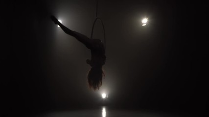 Silhouette young caucasian brunette sportive dancer female balancer in beige leotard back lying hang on aerial hoop on three rays of light background 032