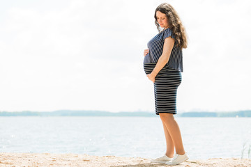 Cheerful pregnant woman with long hair standing on the beach. Happy pregnancy concept.