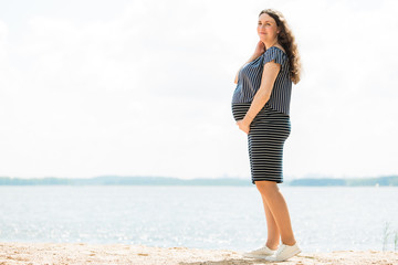 Cheerful pregnant woman with long hair standing on the beach. Happy pregnancy concept.