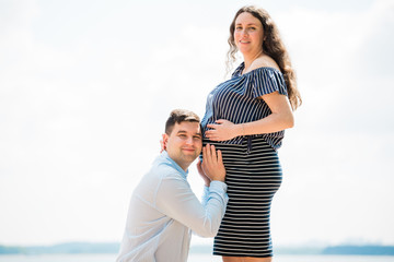 Handsome man is listening to his pregnant wife's tummy. Chherful future dad near belly.  Happy pregnancy concept.