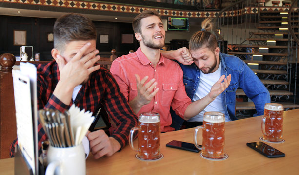 Sad male football fans watching game at bar and drinking beer.